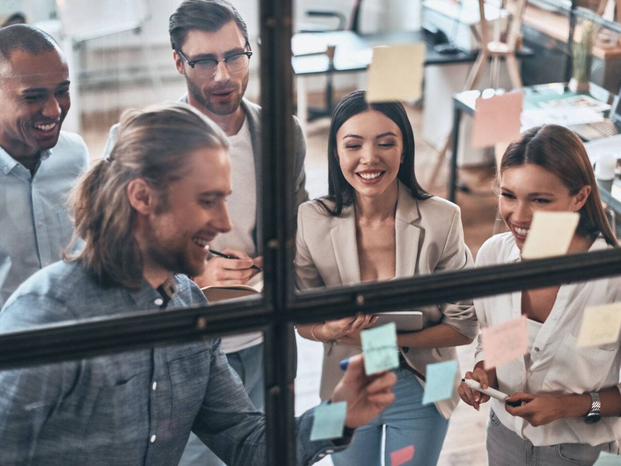 Ensuring success by working as a team. Top view of young modern people in smart casual wear using adhesive notes while standing behind the glass wall in the board room