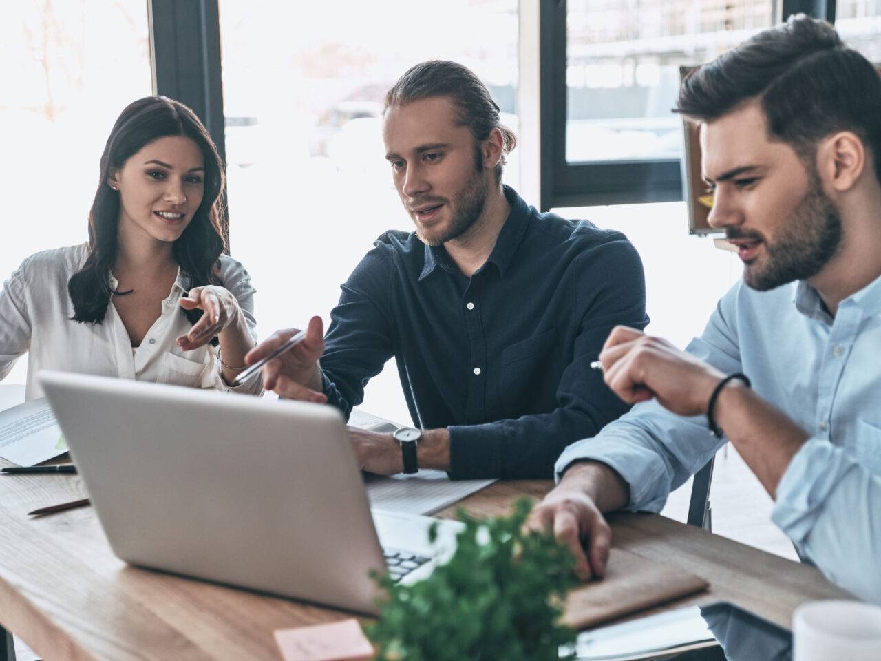 Working day. Group of young modern people in smart casual wear pointing at laptop and smiling while sitting in the creative office